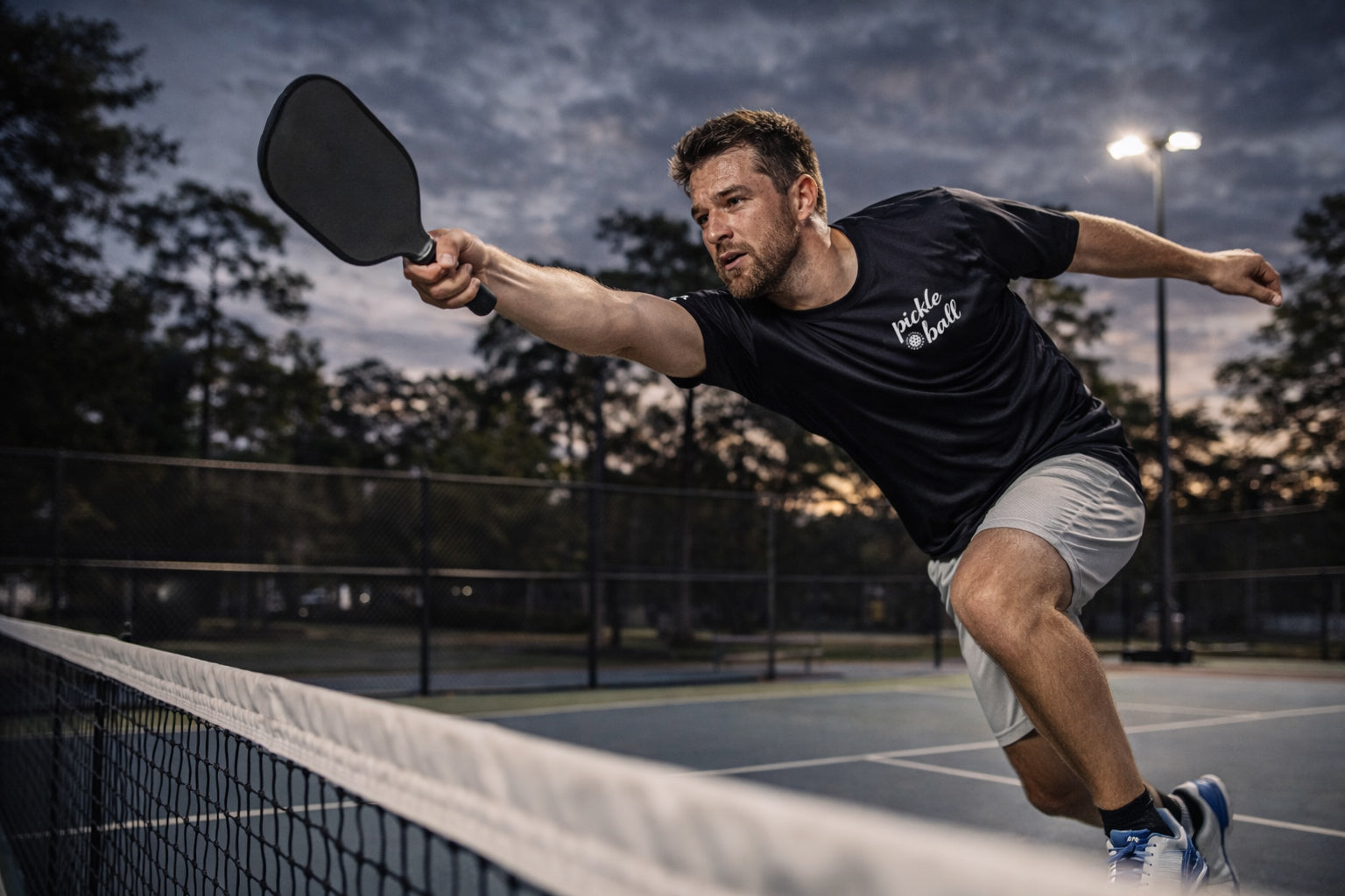 Man playing pickleball on an outdoor court at dusk